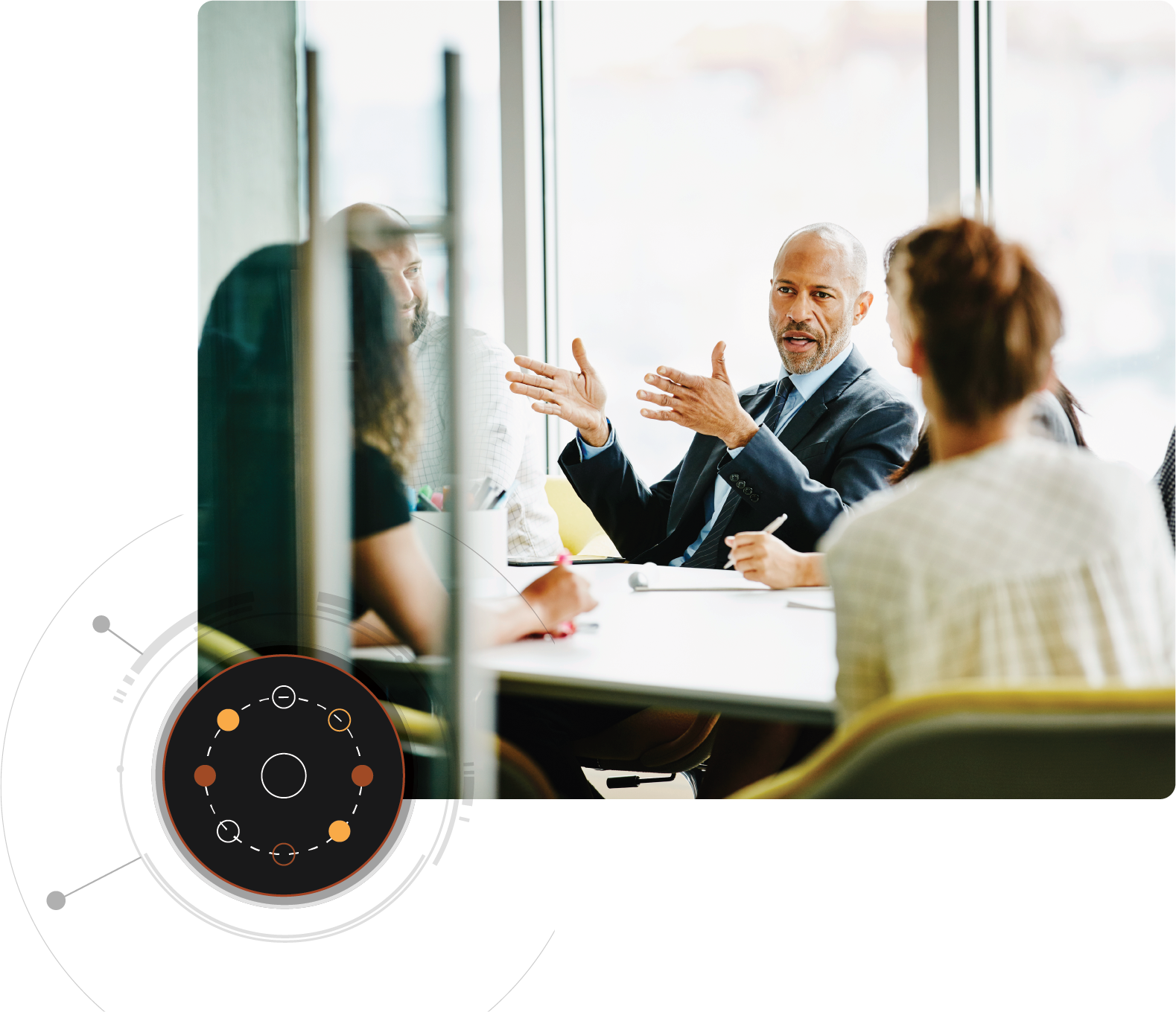 Un hombre está hablando a varias personas reunidas alrededor de una mesa con un gráfico circular superpuesto en la esquina inferior izquierda.